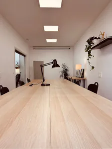 Mesa larga de madera clara con un flexo, vista de frente.