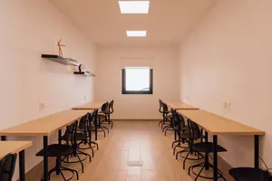 Sala polivalente con dos filas de mesas y sillas, como un aula.