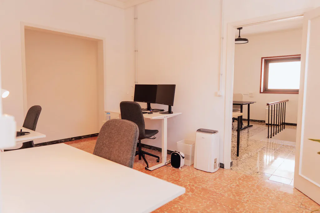 Zona de puestos con monitores y una puerta abierta a otra sala.
