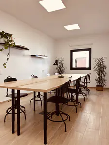 Sala polivalente con mesas largas, taburetes y plantas.